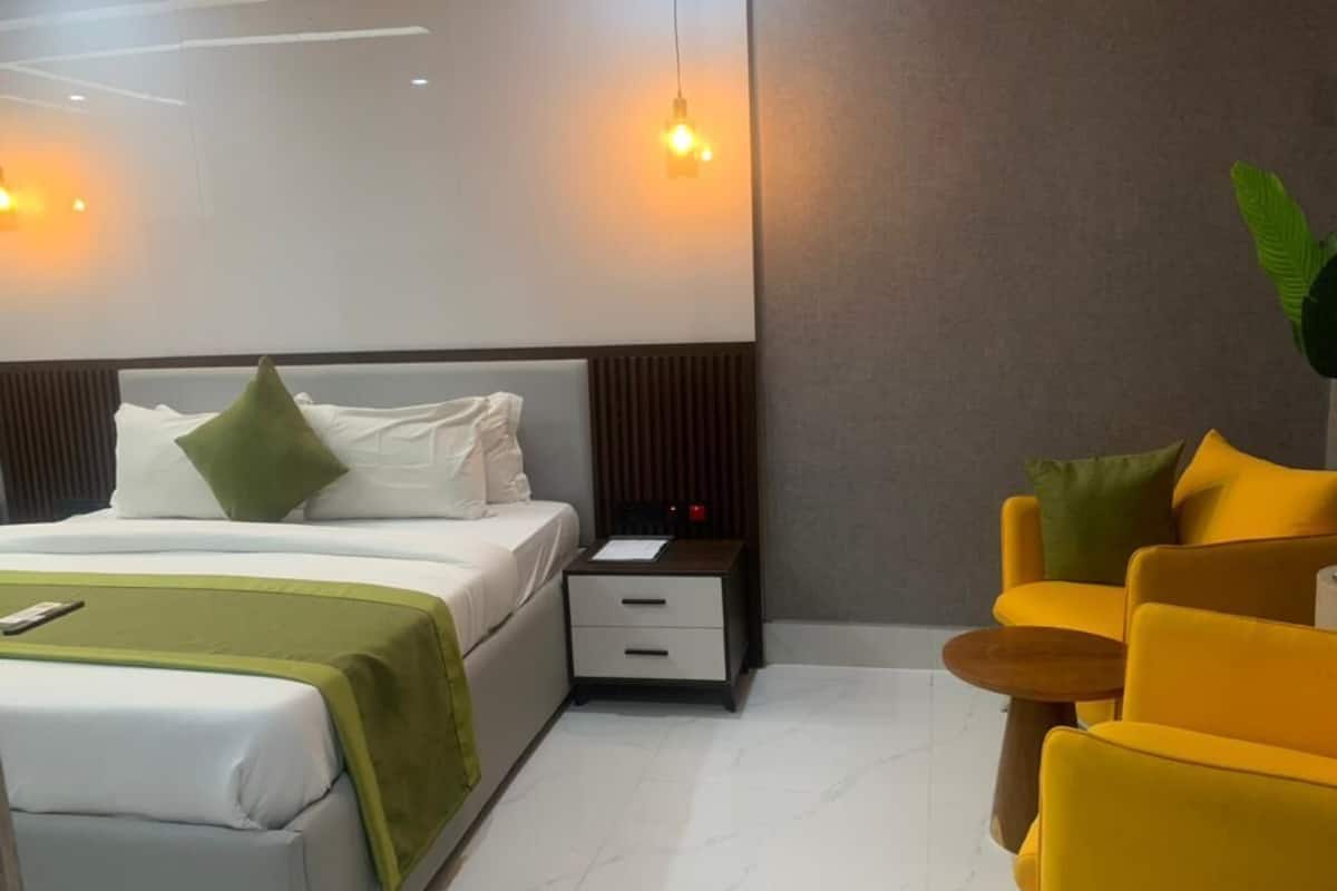 Une chambre d’hôtel moderne avec un lit, une table de chevet et un fauteuil jaune.