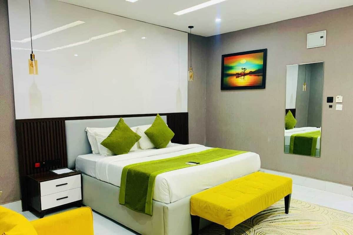 Une chambre à coucher moderne avec un grand lit, une table de chevet, un banc, un miroir et un tableau accroché au mur.