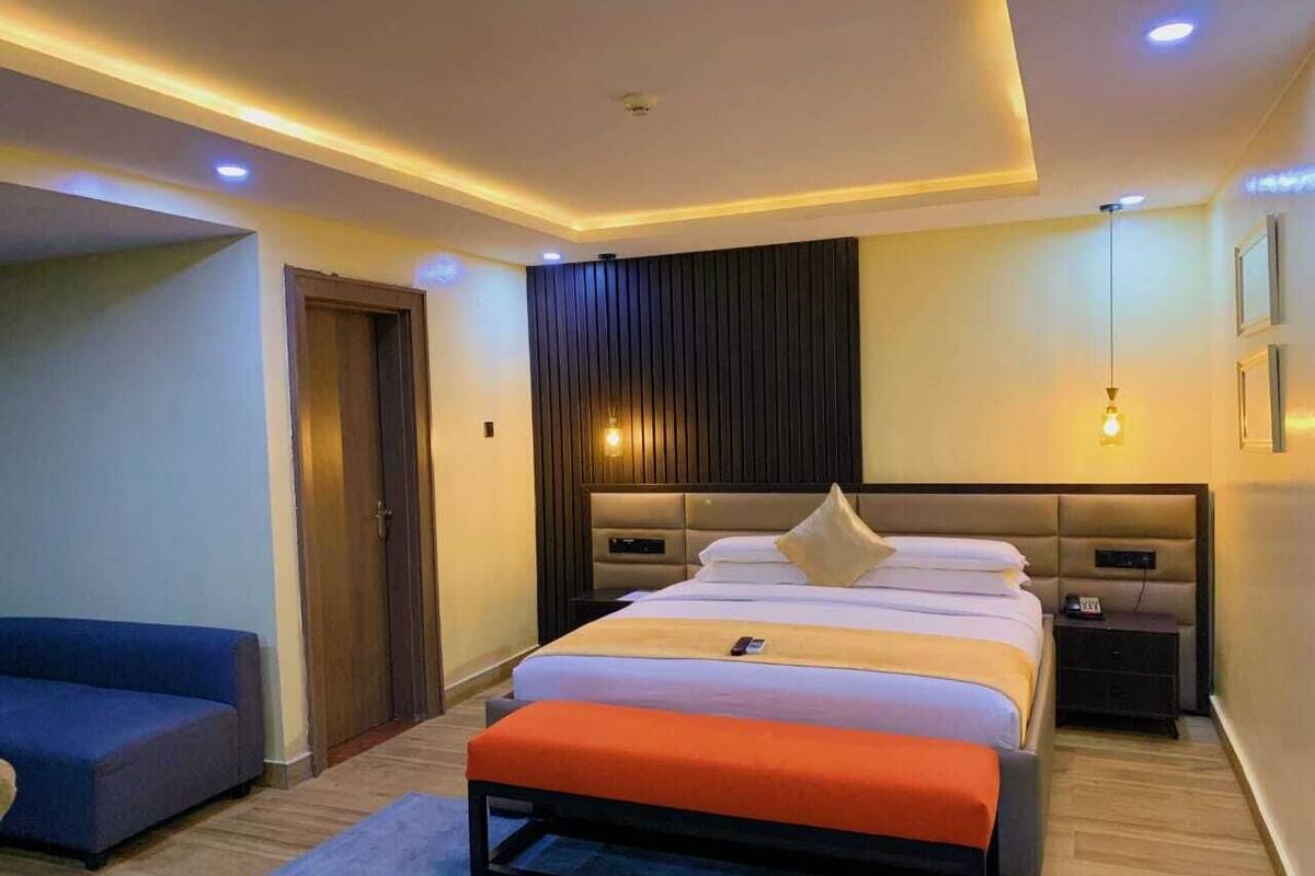 Une chambre d’hôtel moderne avec un grand lit, une table de chevet, une commode, un canapé et une porte.