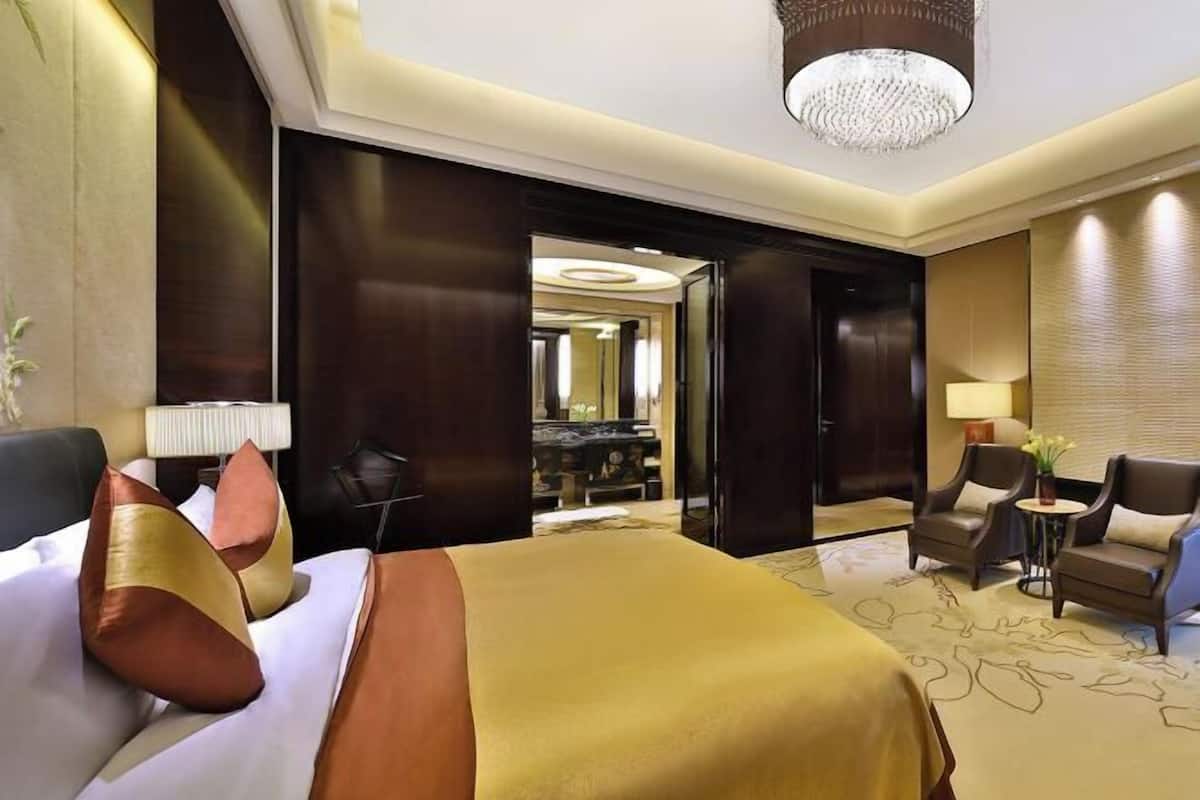 Ein Hotelzimmer mit einem großen Bett, einer Sitzecke mit Stühlen, einem kleinen Tisch und einem Spiegel.