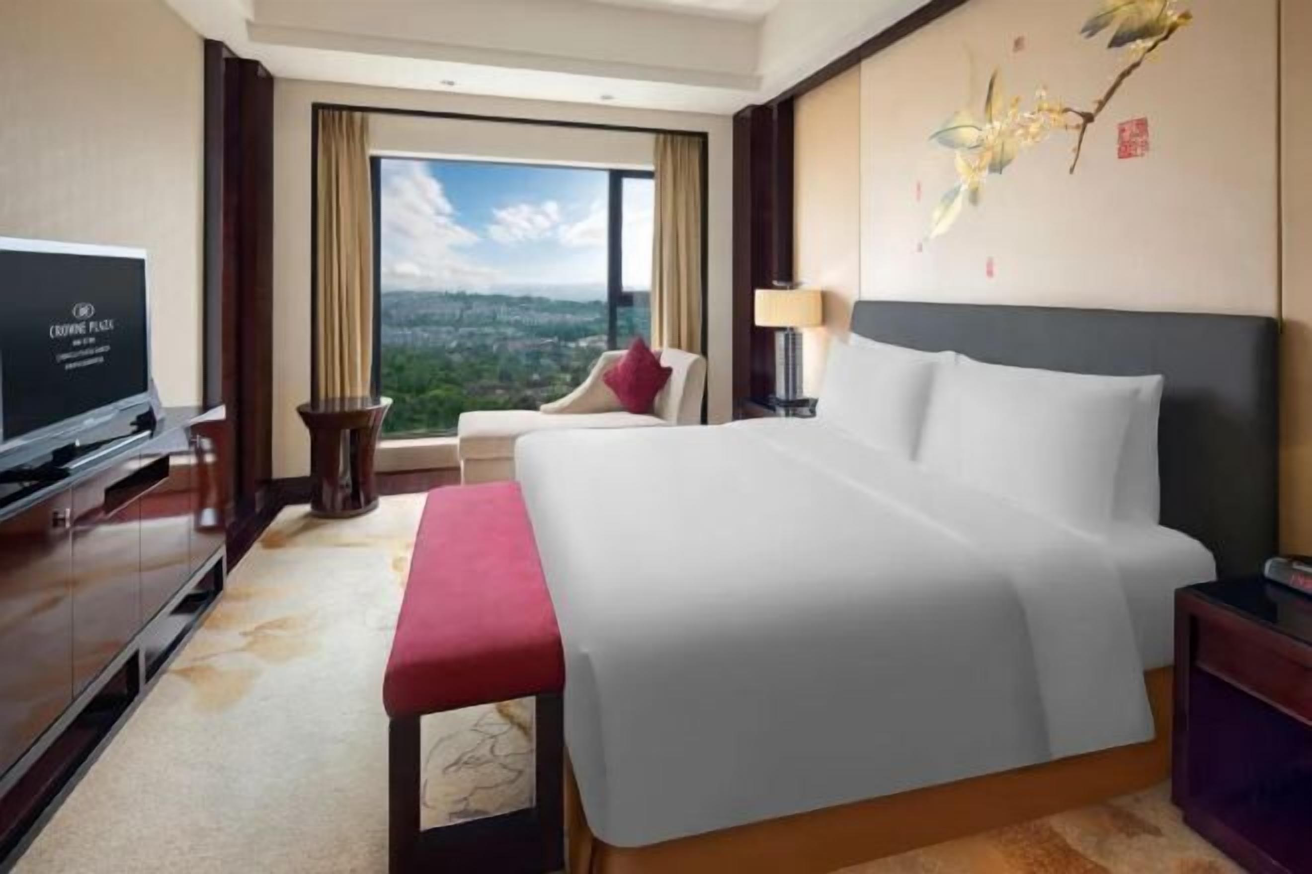 Une chambre d’hôtel avec un grand lit, une télévision, une chaise, un bureau et une vue sur la ville.