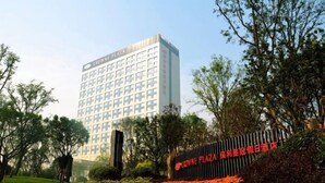 Un hotel con fachada moderna, una entrada destacada y un jardín bien cuidado con flores de naranja.