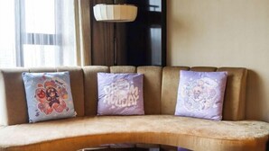 Un sofá con tres almohadones decorativos, una lámpara colgante y una ventana con cortinas.