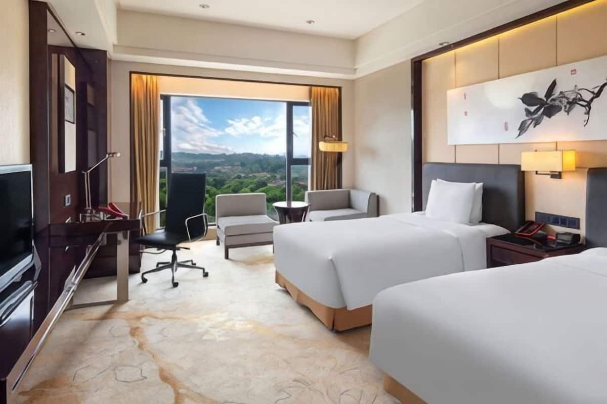 Ein Hotelzimmer mit zwei Betten, einem Schreibtisch, einem Sessel, einem Fernseher und einem großen Fenster mit Blick.
