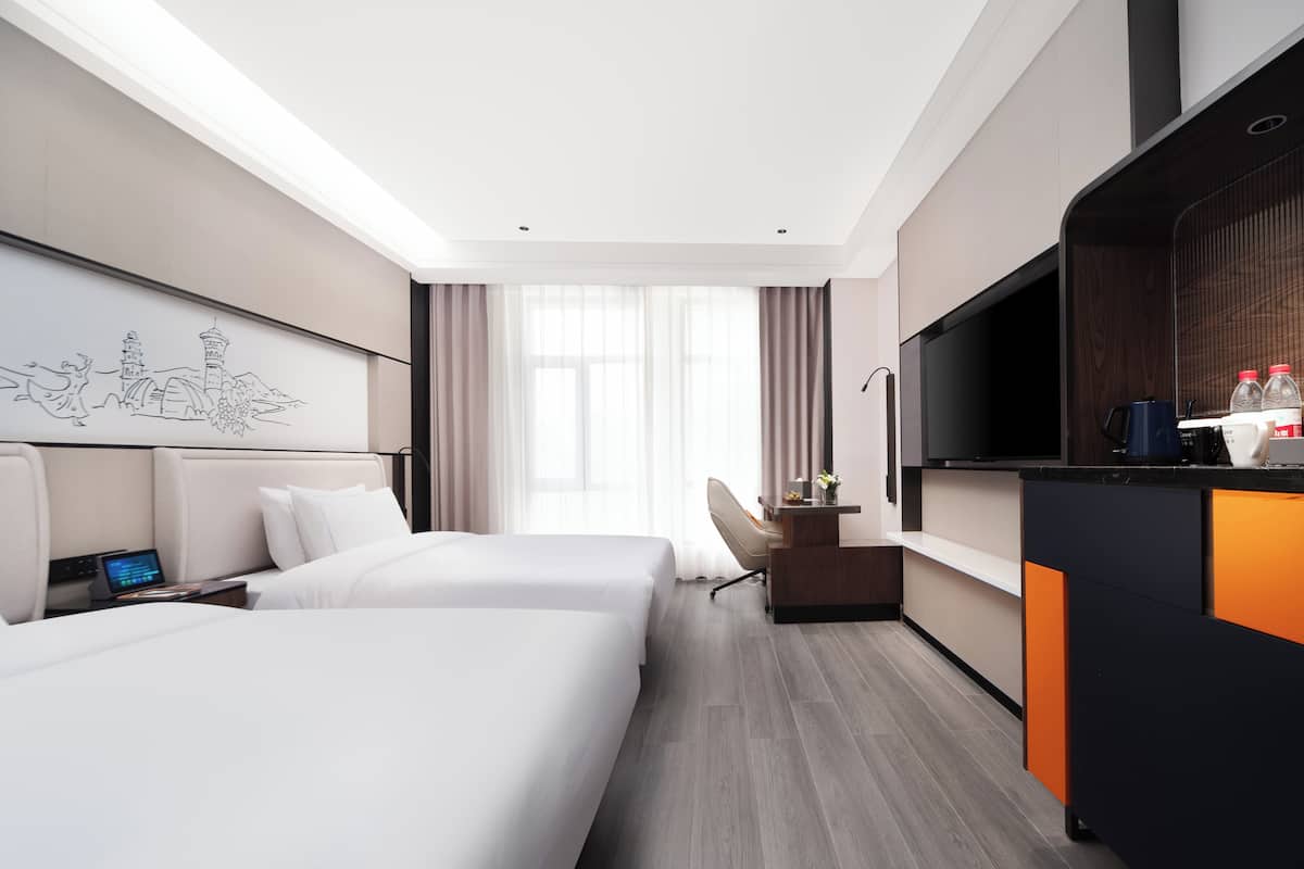 Une chambre d’hôtel avec deux lits, un bureau, une télévision et une œuvre d’art représentant un paysage urbain accrochée au mur.