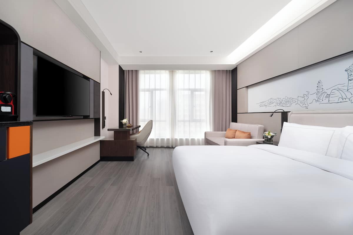 Une chambre d’hôtel moderne dotée d’un grand lit, d’un bureau avec un téléviseur à écran plat, d’une chaise et d’une lampe de bureau.