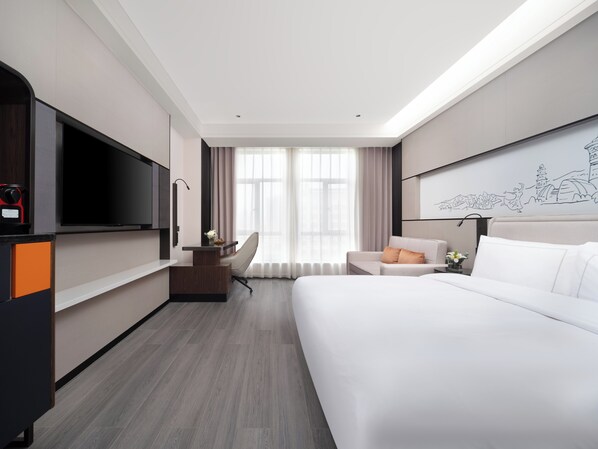 Una habitación de hotel moderna con una cama grande, un escritorio con televisor de pantalla plana, una silla y una lámpara de escritorio.