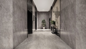 A modern hallway with grey marble walls, a central potted plant, and a small table with a vase. - UrCove by Hyatt Aksu Century Square (Aksu)