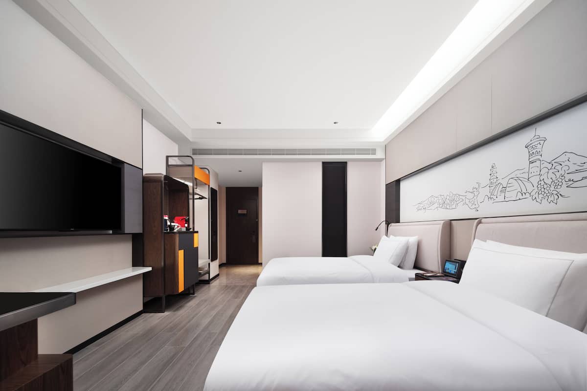 Une chambre d’hôtel moderne équipée de deux lits, d’un téléviseur à écran plat, d’un bureau et d’une grande fenêtre.