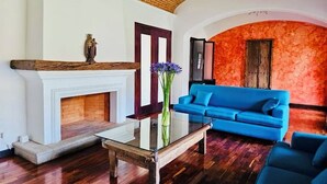 Una sala de estar con chimenea, sofá azul y una mesa de centro de vidrio.