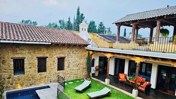 Un edificio de piedra con piscina, un porche cubierto con sillones de descanso y vistas del paisaje circundante.