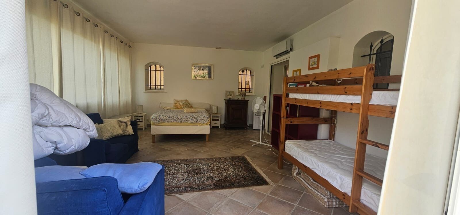 A room with a bed, a bunk bed, a sofa, a desk, and a window with curtains.