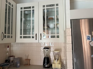 Una cocina con armarios blancos, un refrigerador de acero inoxidable, una licuadora y una botella de vino.