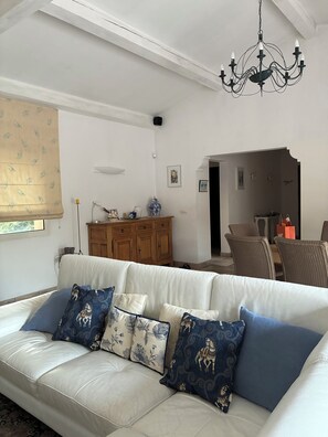 A living room with a sofa, cushions, a chandelier, a cabinet, and a dining area. - Villa in Saint Jeannet in the Nice hinterland; sleeps 10; fenced-in garden (Saint-Jeannet)