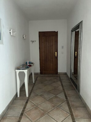 A hallway with a wooden door, a white table with books, and a tiled floor.