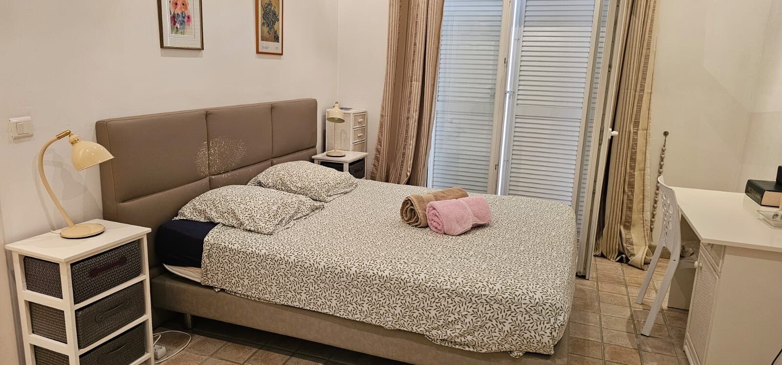 Une chambre à coucher avec un lit, des tables de chevet, un bureau et une fenêtre avec des rideaux.