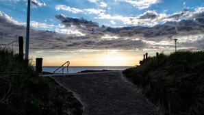 Een verhard pad dat naar een strand leidt, met een zonsondergang op de achtergrond.