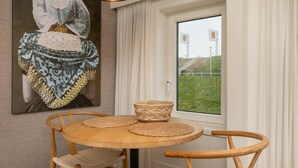 A dining area with a round wooden table, two woven placemats, and a woven bowl. A painting of a person in traditional attire hangs on the wall. - Apartment in Zeeland Near the Beach (Zoutelande)