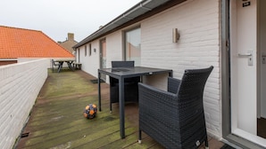A balcony with a table and chairs, a door with a number, and a red-tiled roof in the background. - Apartment in Zeeland Near the Beach (Zoutelande)