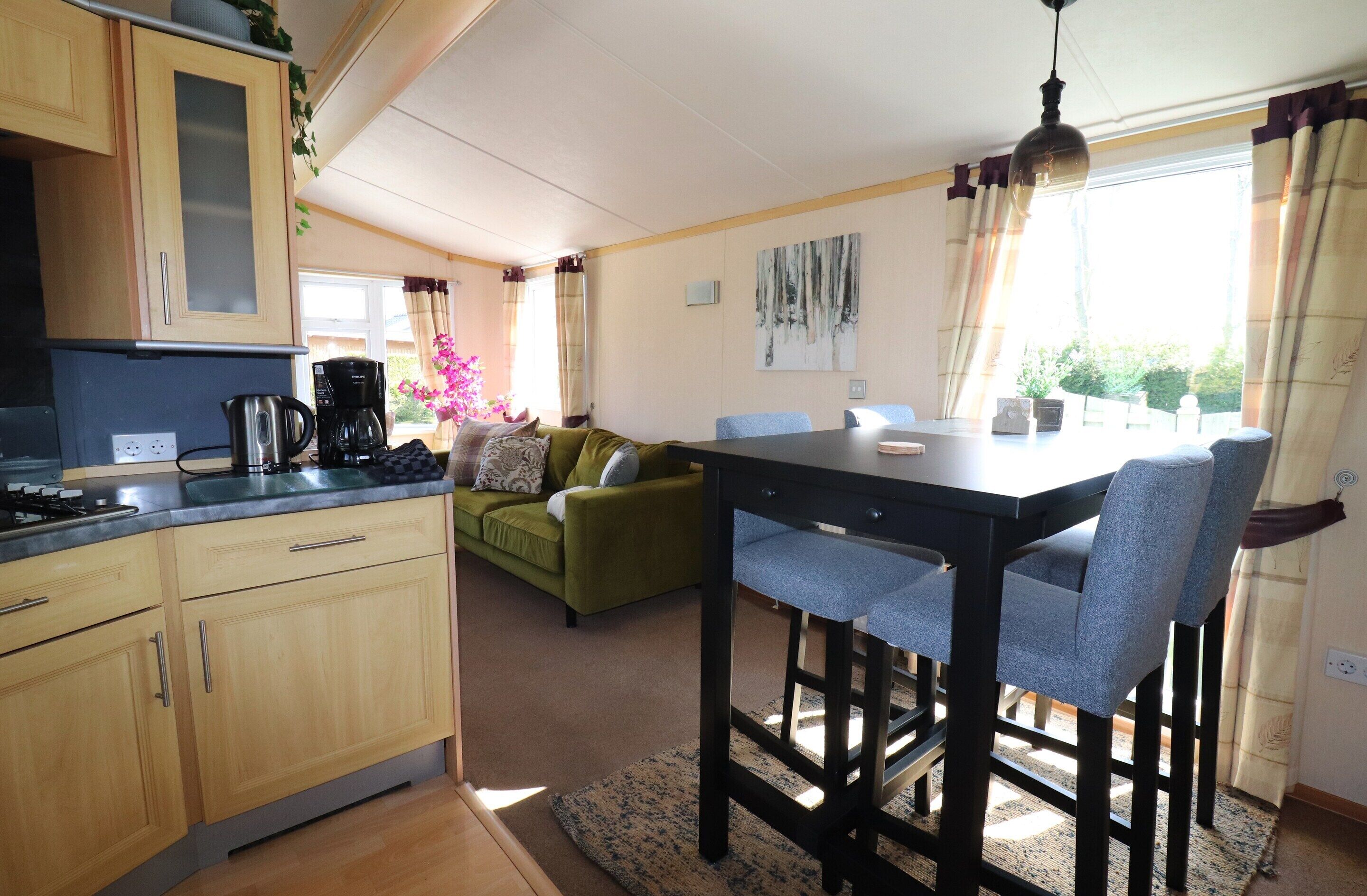 A compact kitchen with wooden cabinets and a coffee maker, a dining area with a table and chairs, and a green sofa.
