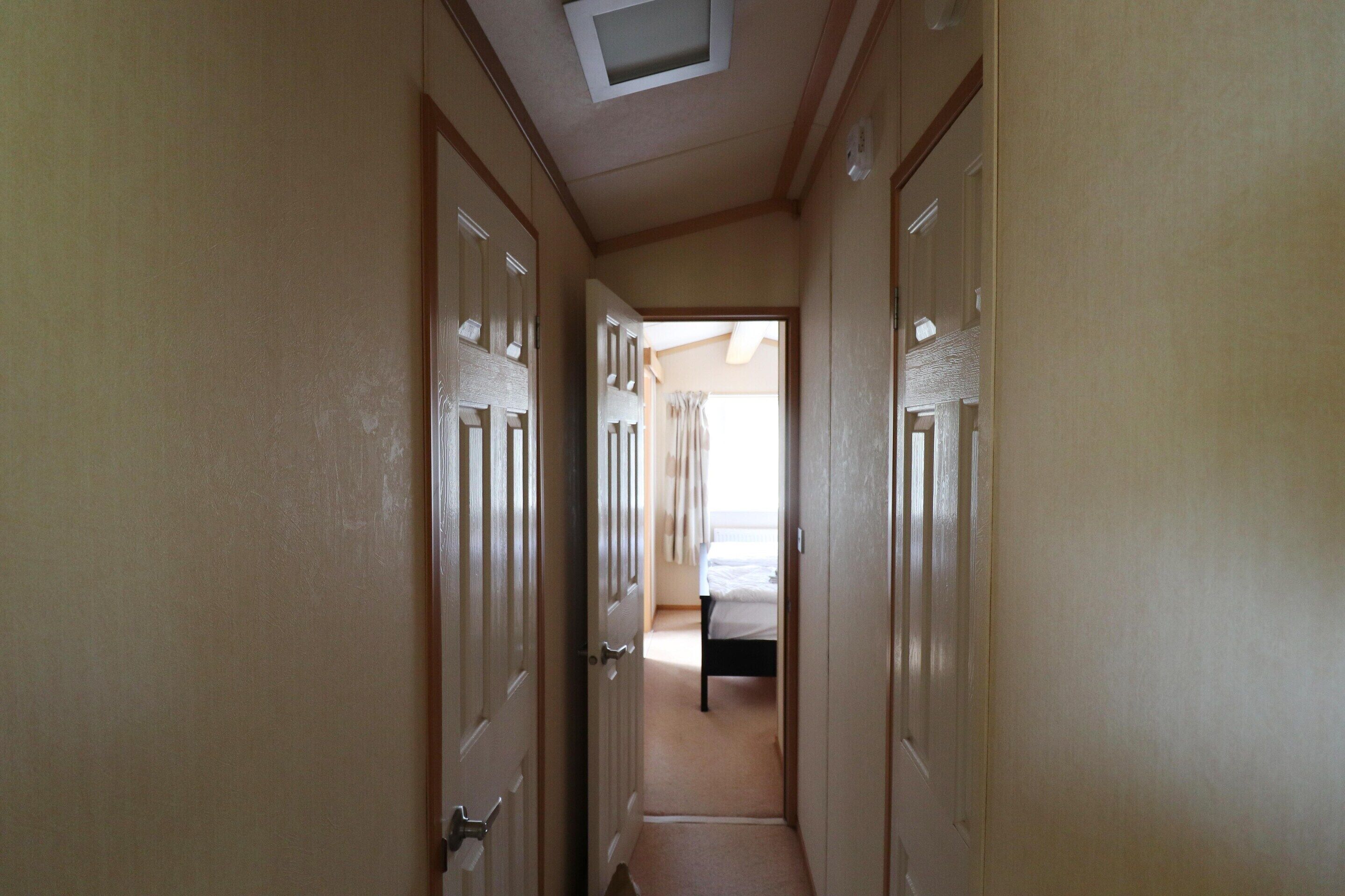 Un pasillo estrecho con puertas a ambos lados que dan a un dormitorio con cama y ventana.