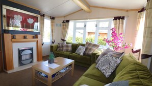 A cozy living room with a green sofa set, a wooden coffee table, and a fireplace. - Cozy Chalet in Tzummarum (Tzummarum)