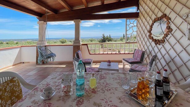 A terrace with a table set for dining, a hanging chair, and a view of the landscape. - IN OROSEI APARTMENT WITH SEA VIEW VERANDA (OROSEI)