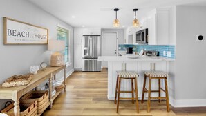 A modern kitchen with white cabinets, a stainless steel refrigerator, a microwave, and a blue-tiled island with bar stools. - Book Magnolia Shores: Family-Friendly Getaway Near Beach with Pool and Mini Golf (Anna Maria)