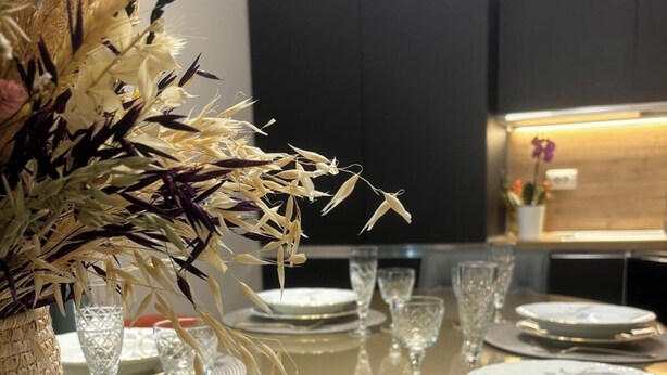A dining table set with plates, glasses, and a decorative vase with dried plants. There are two books titled 'Roma' and 'Sentieri Roma'.