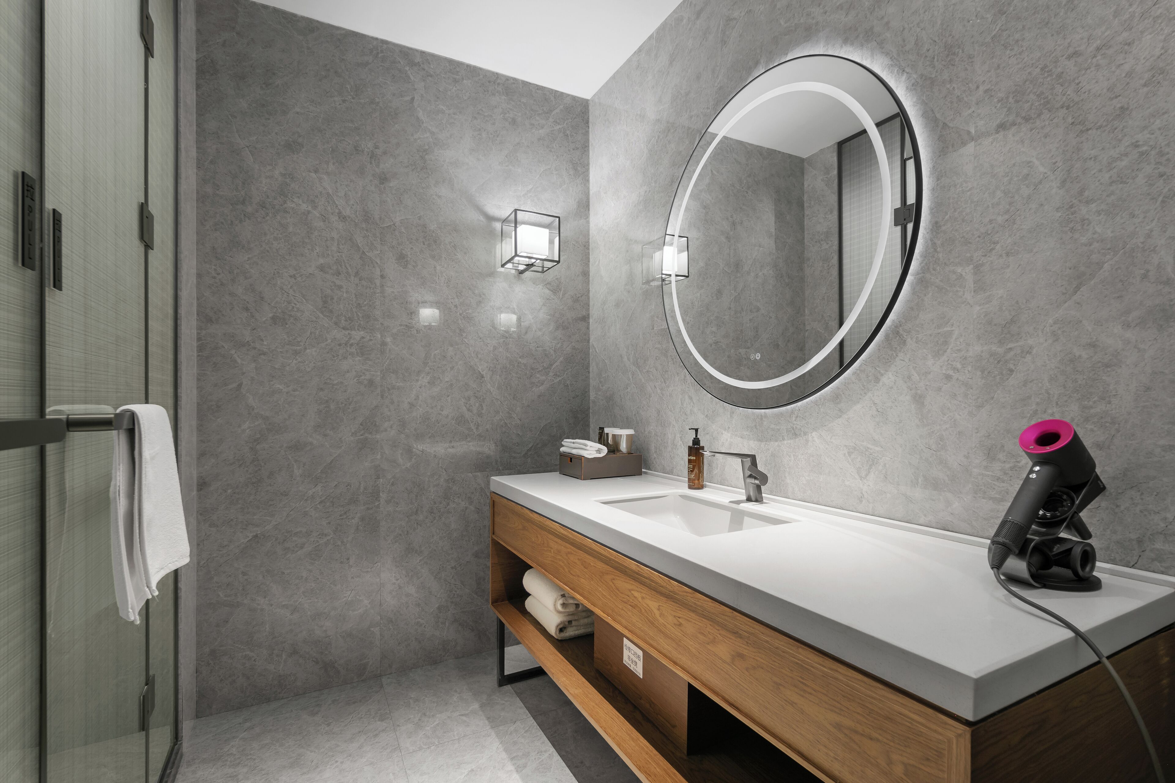 A modern bathroom with a large mirror, a white sink, and a hairdryer on the counter.
