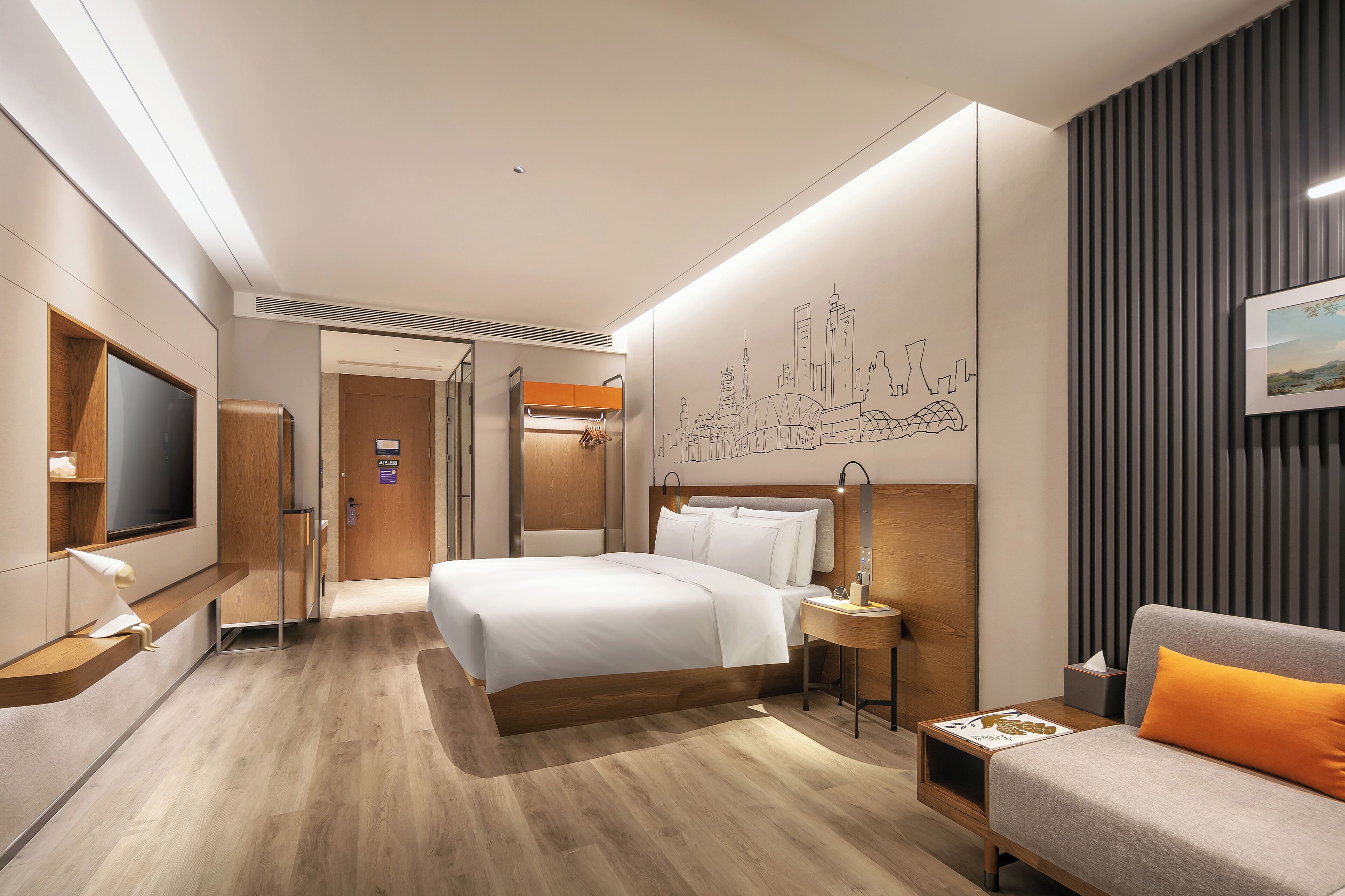 Een moderne hotelkamer met een groot bed, een bank, een televisie en een stadsgezicht muurschildering.