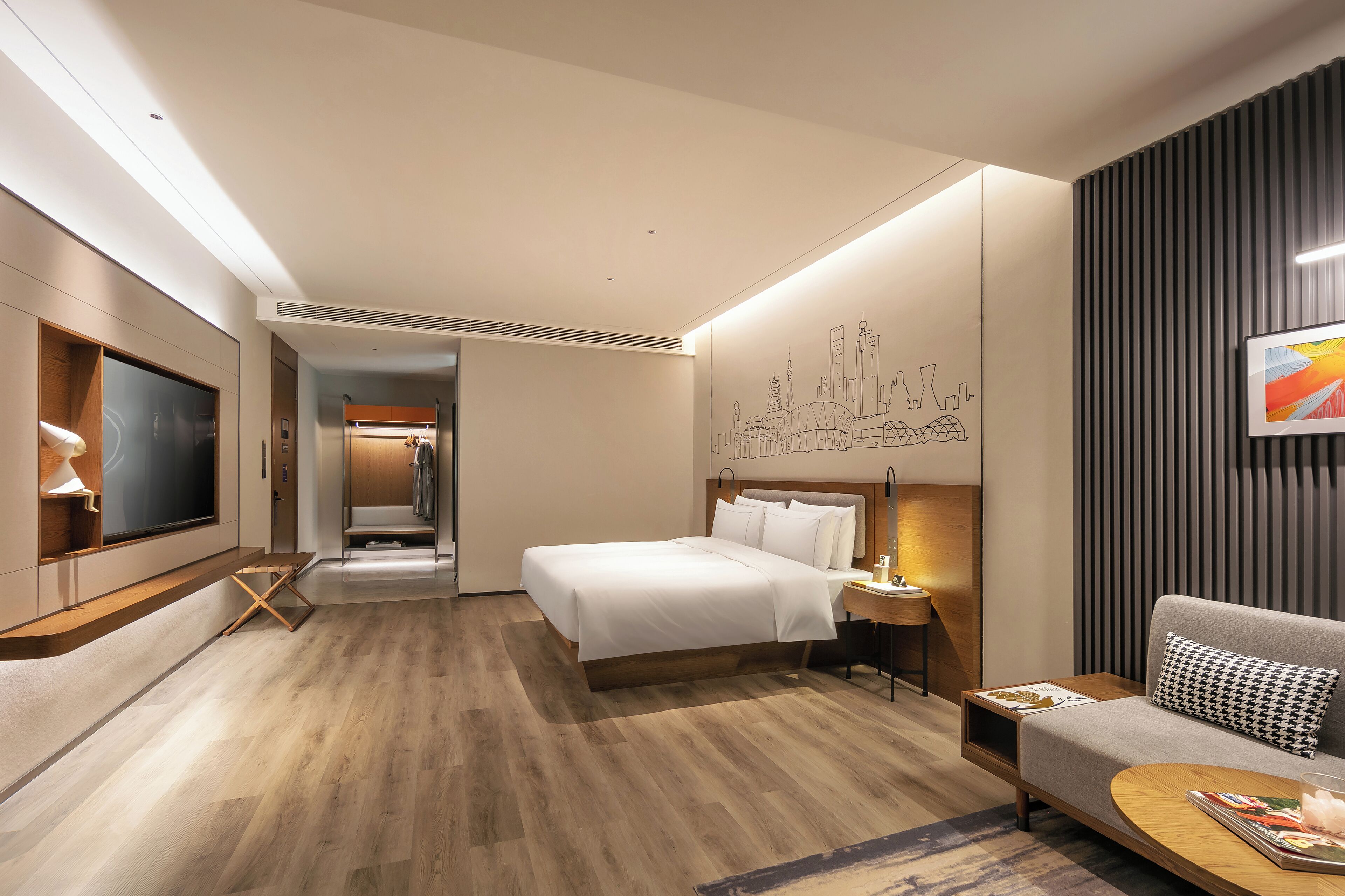 A modern hotel room with a large bed, a sofa, a TV, and a desk.