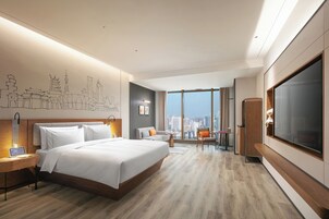 Una habitación de hotel moderna con una cama grande, un escritorio con una computadora portátil, un televisor y vistas a la ciudad.