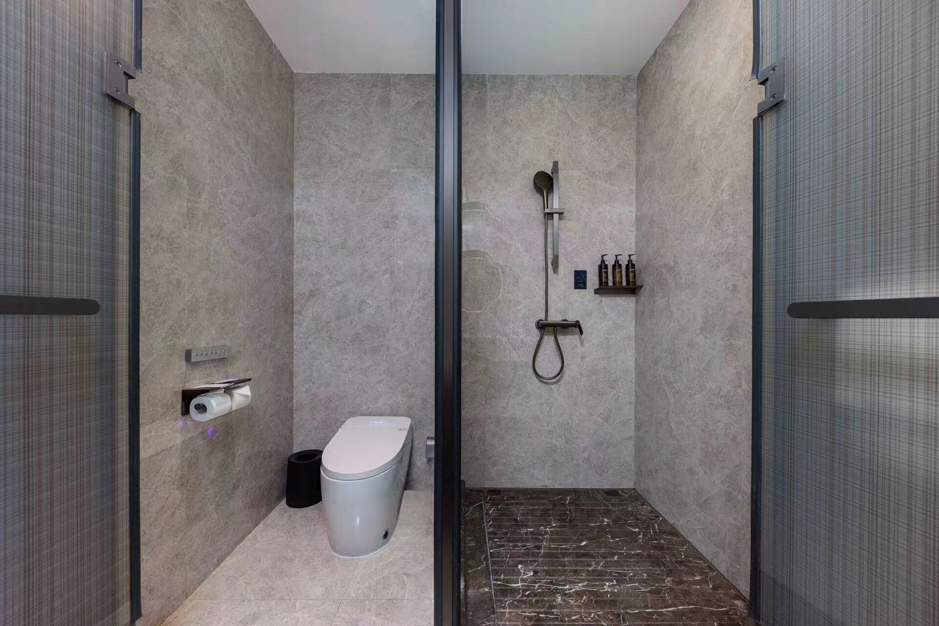A modern bathroom with a shower, toilet, and a marble floor.