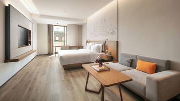 Une chambre d’hôtel comprenant un lit, un canapé, une télévision, un bureau et une œuvre d’art murale.