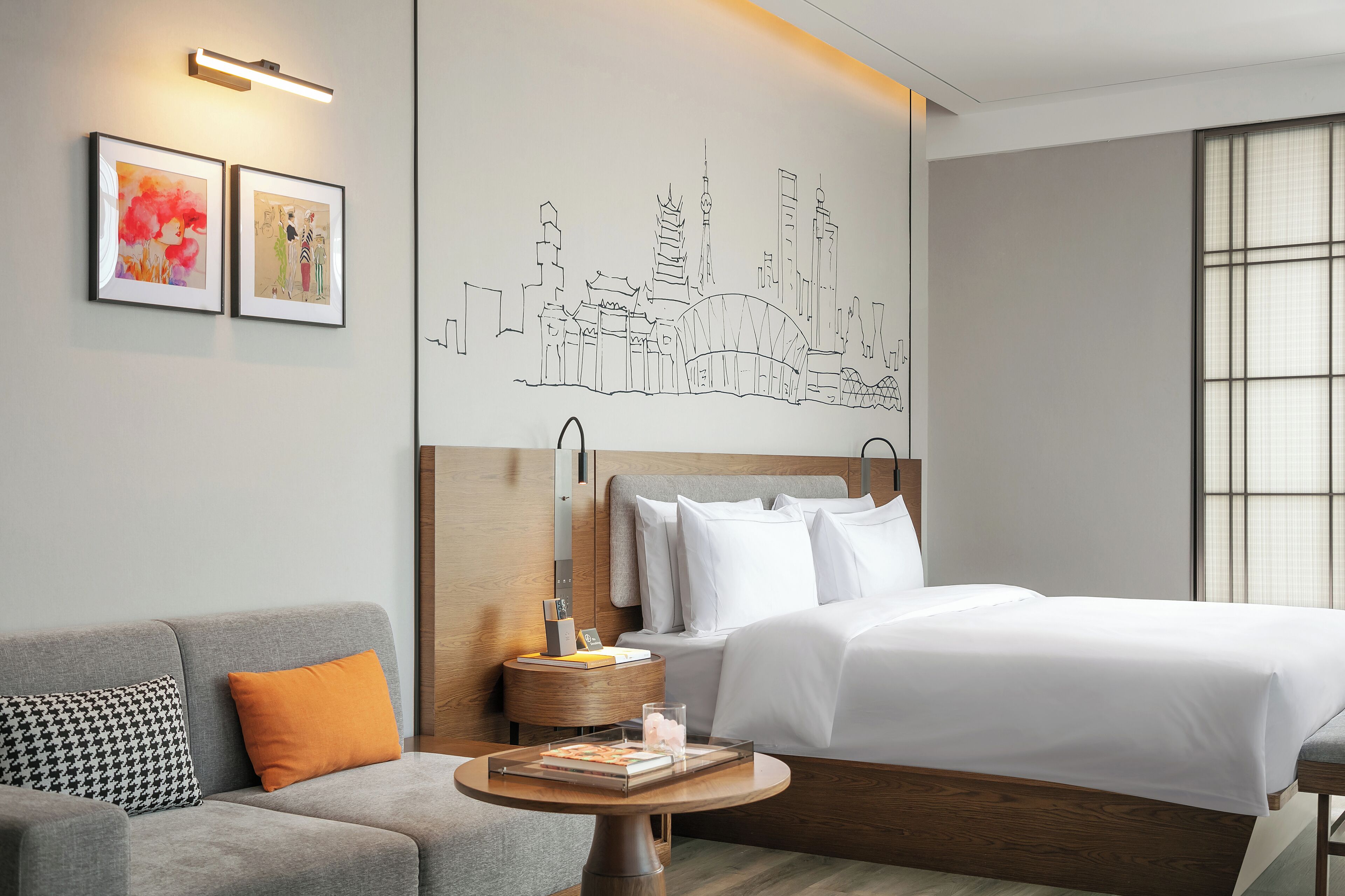 A hotel room with a bed, a sofa, a round table, and artwork on the wall.