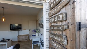 A cozy living room with a TV, a dining area, and a wooden sign with directional words like "beach" and "coast." - Penthouse Near Koksijde Beach (Middelkerke)