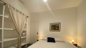 Une chambre à coucher avec un lit, une armoire, une porte, une table de chevet avec une lampe et un tableau au mur.