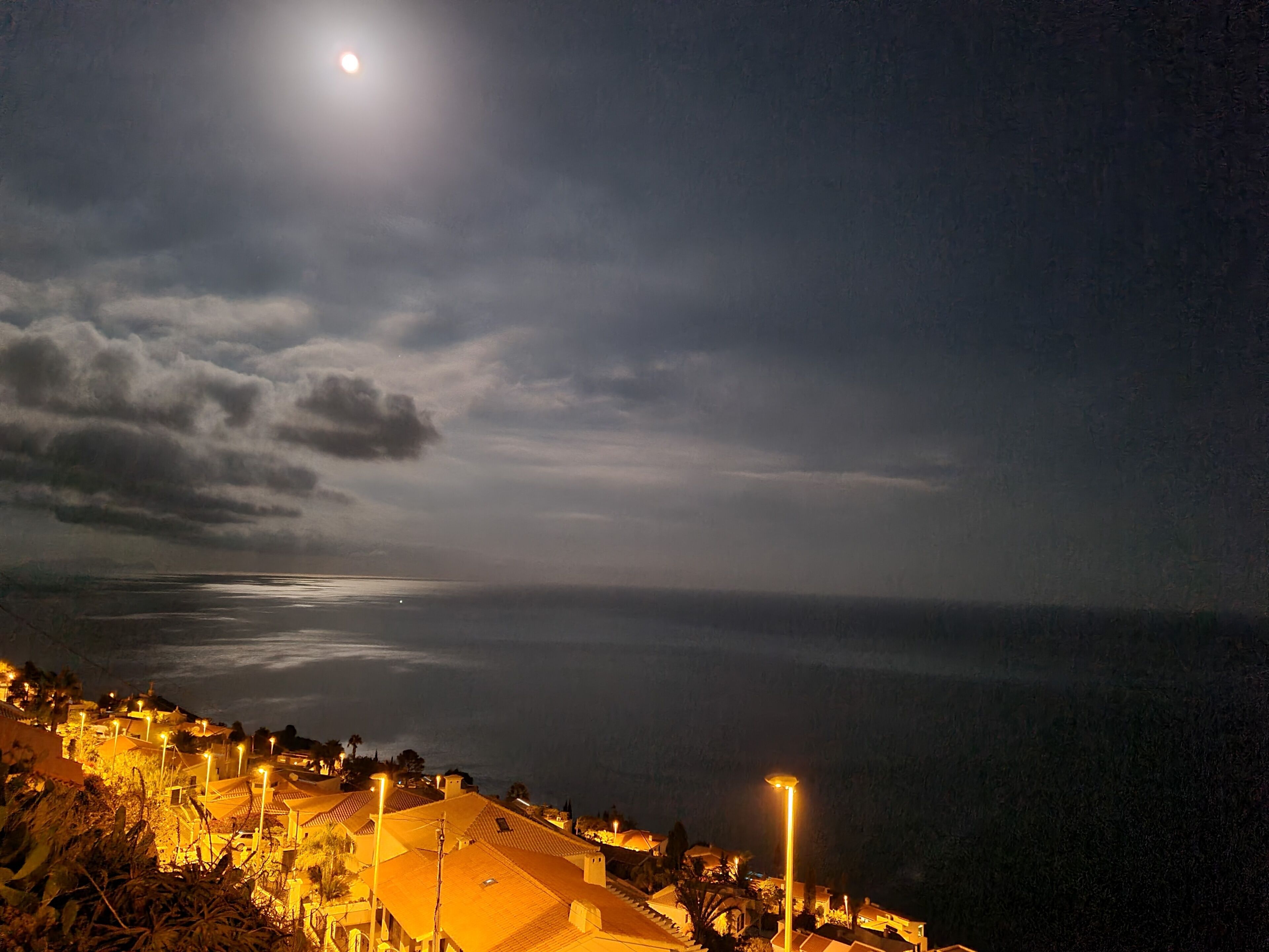A coastal town at night with a visible moon, streetlights, and buildings with sloped roofs.