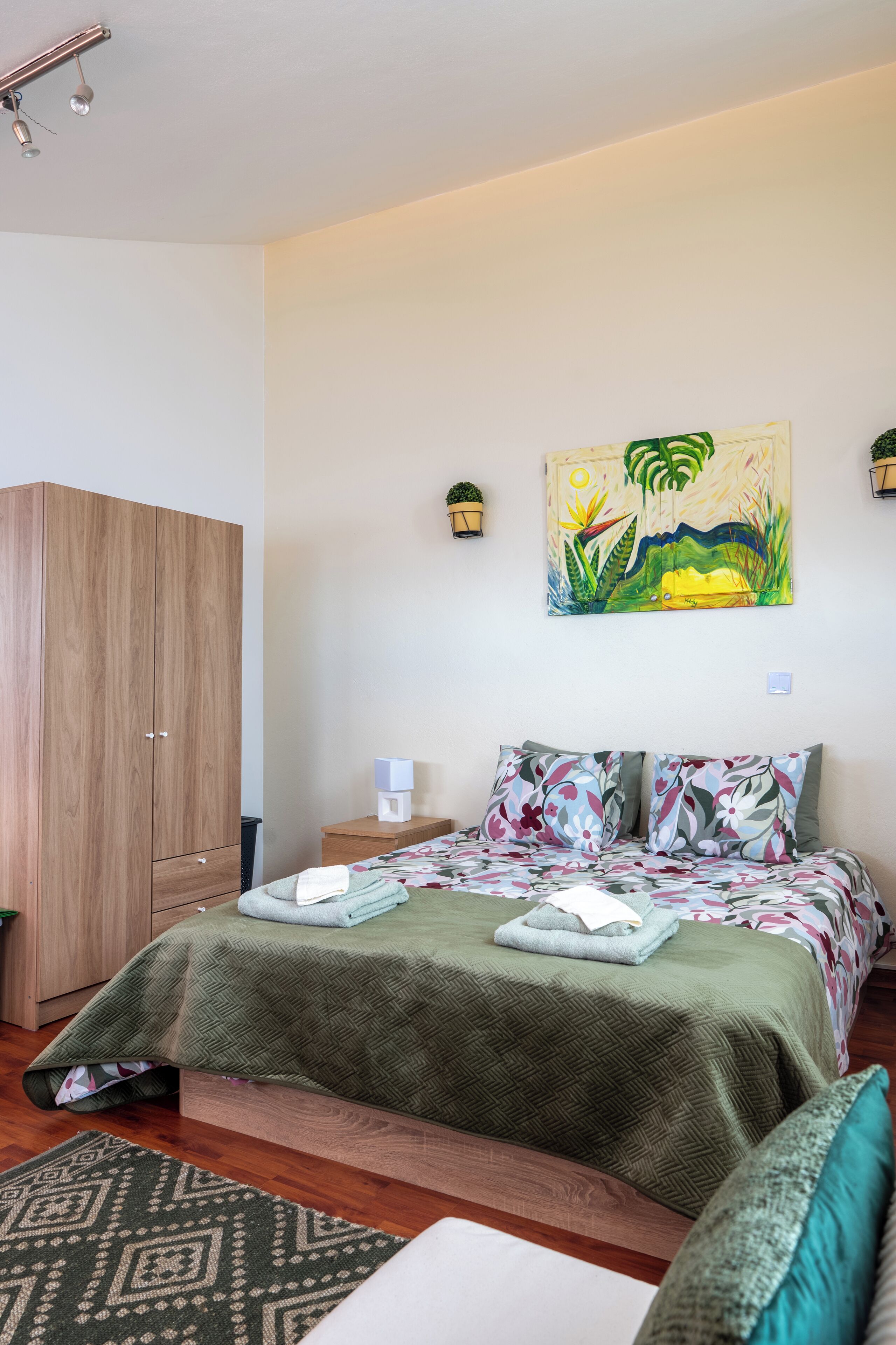 A bedroom with a bed, a wardrobe, a painting, and a nightstand.