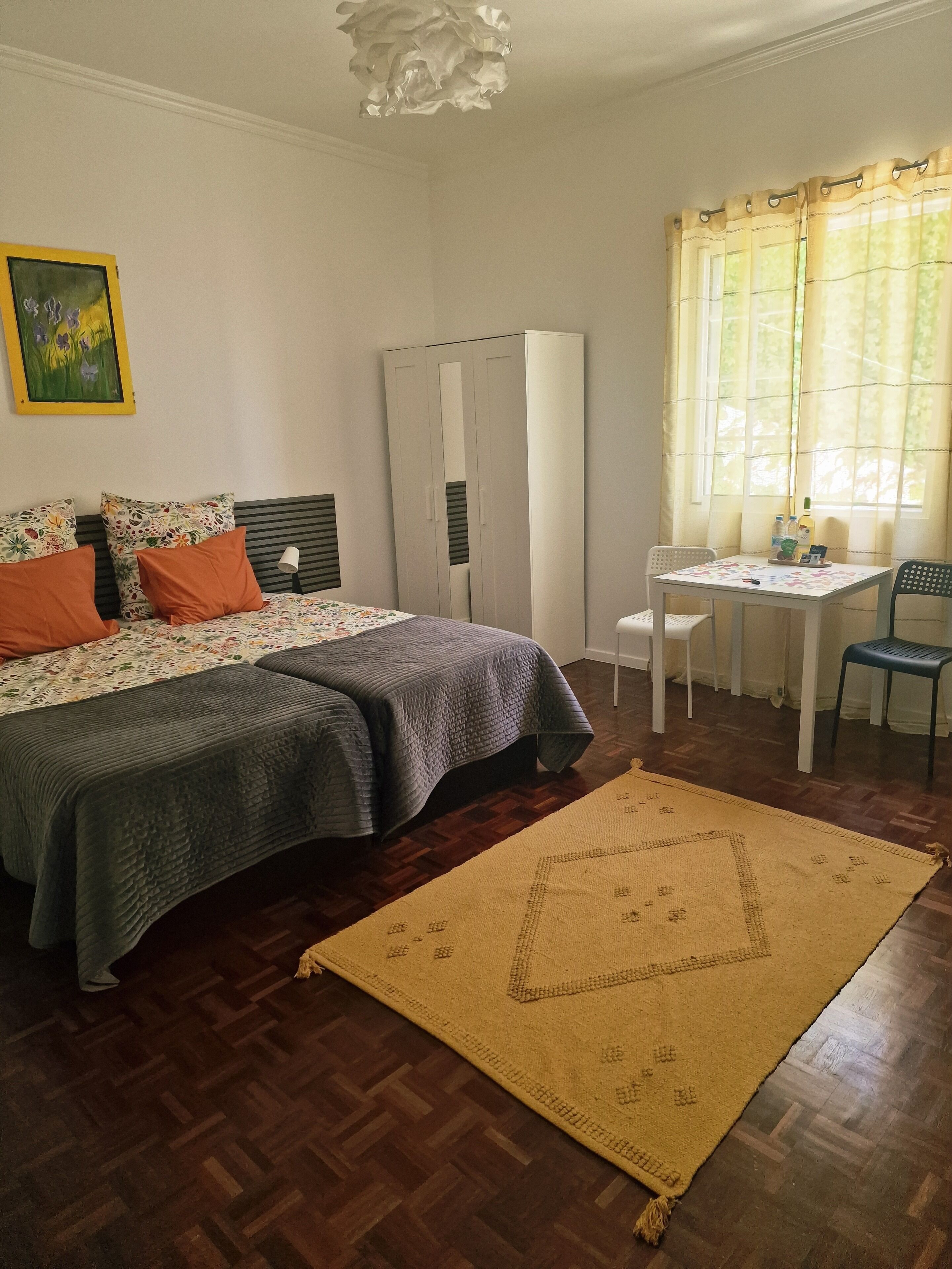A bedroom with a bed, bedside table, chair, wardrobe, and a window with curtains.