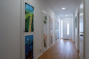 A hallway with wooden flooring and white walls, featuring framed artworks on the left side.