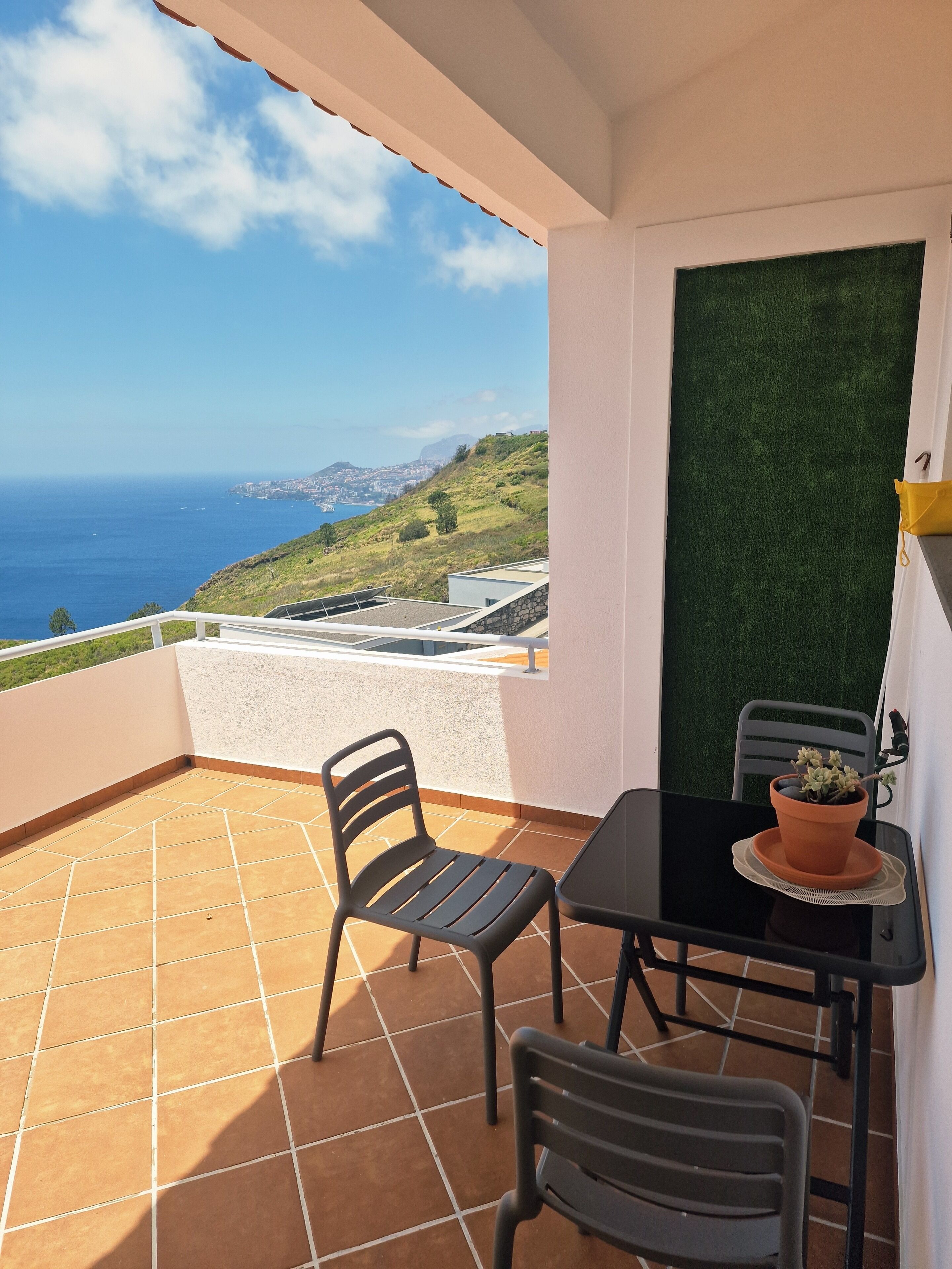 Un balcone con vista sul mare, un tavolo con sedie e una pianta in vaso.