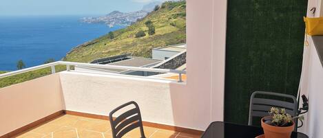 Un balcone con vista sul mare, un tavolo con sedie e una pianta in vaso.