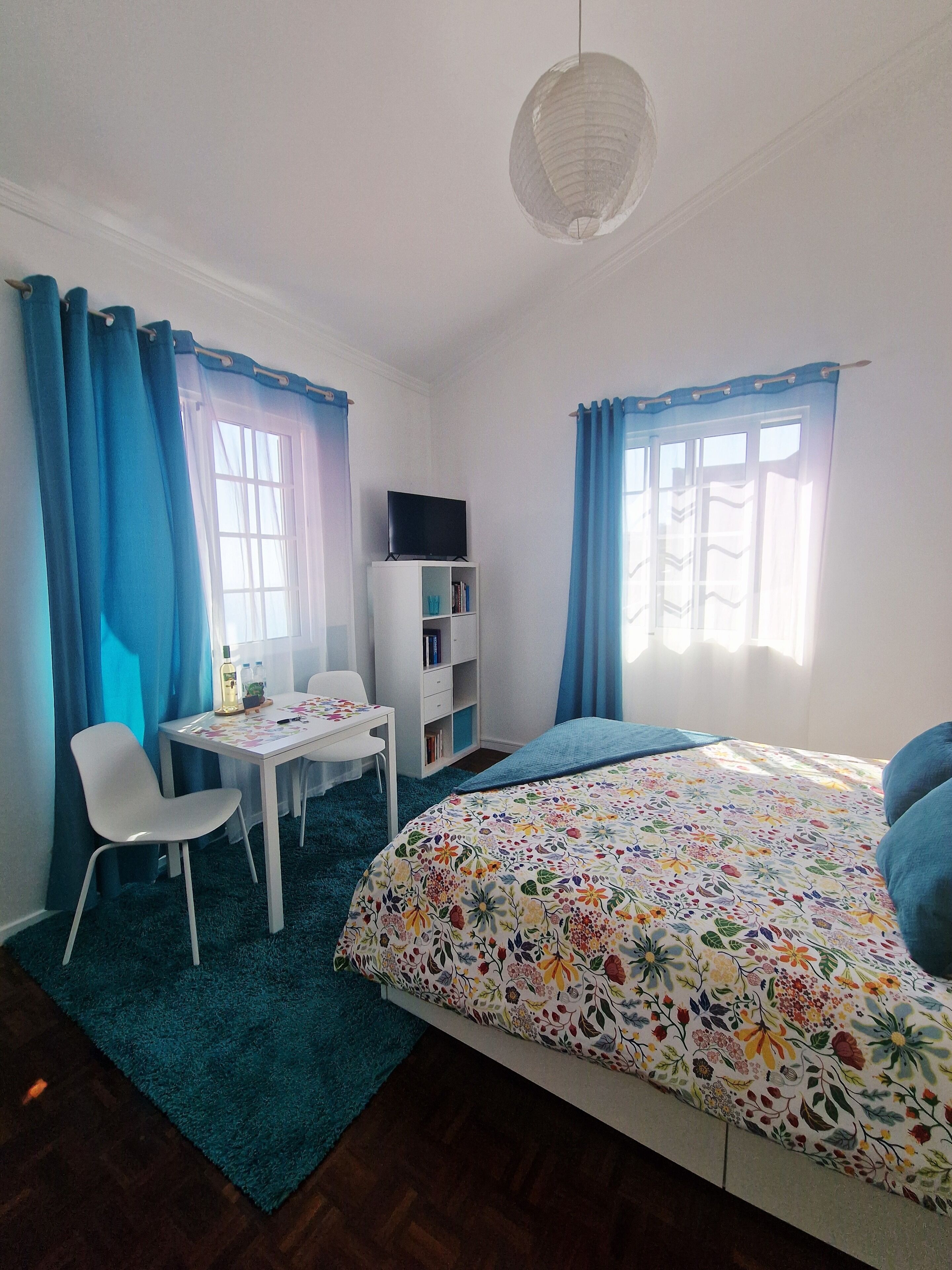 A bedroom with a bed, a desk, a chair, a bookshelf, and a TV.