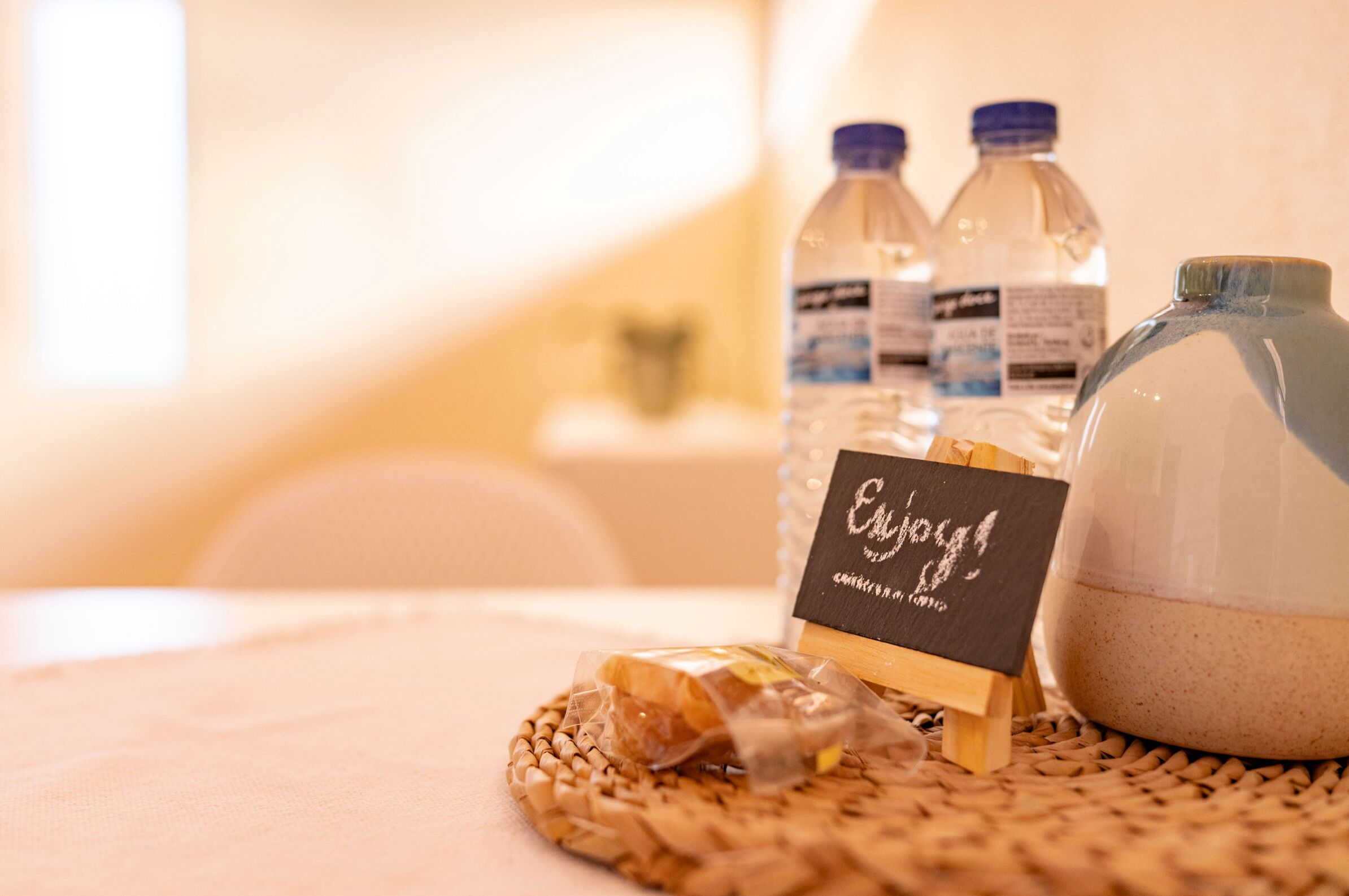 A wicker tray with a small wooden stand holding a sign, a jar of sand, and a plastic bag with a bar of soap.