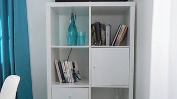 A white bookshelf with teal storage drawers, a white chair, and a blue curtain.