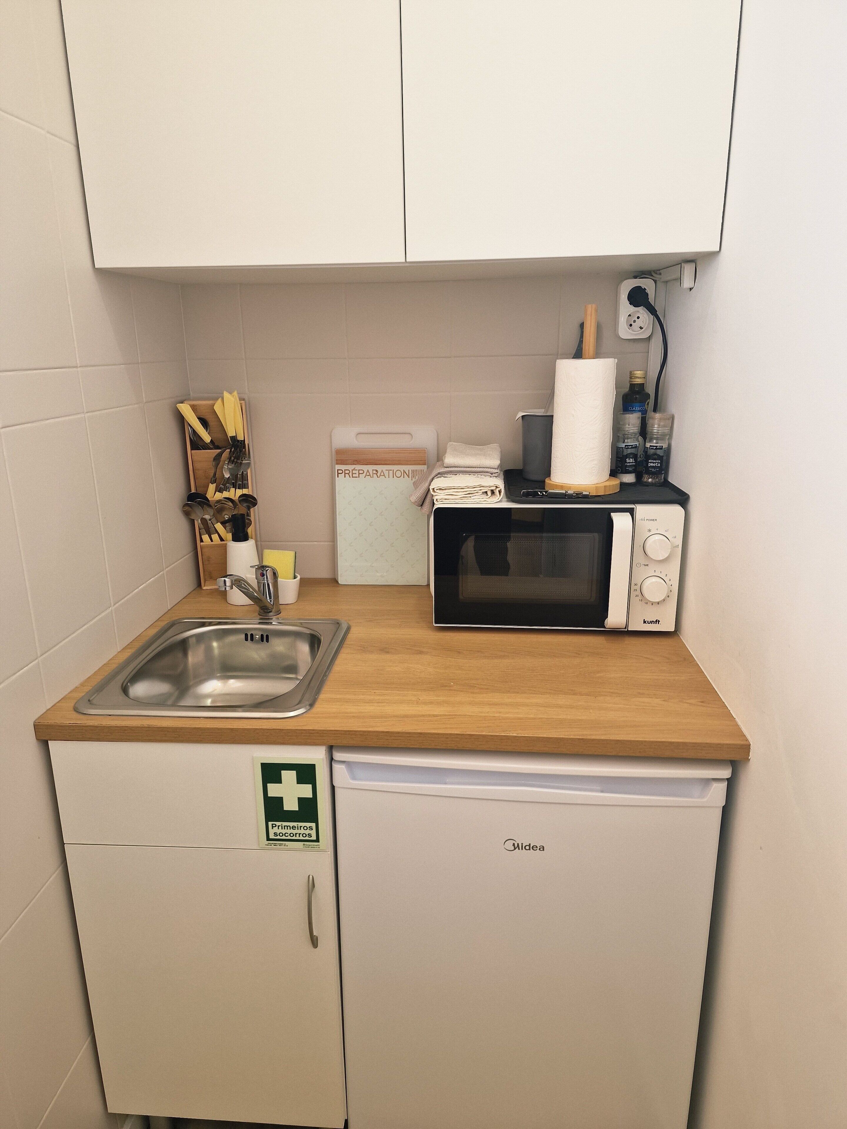 A compact kitchenette with a microwave, sink, and a small cabinet.