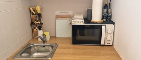 A compact kitchenette with a microwave, sink, and a small cabinet.