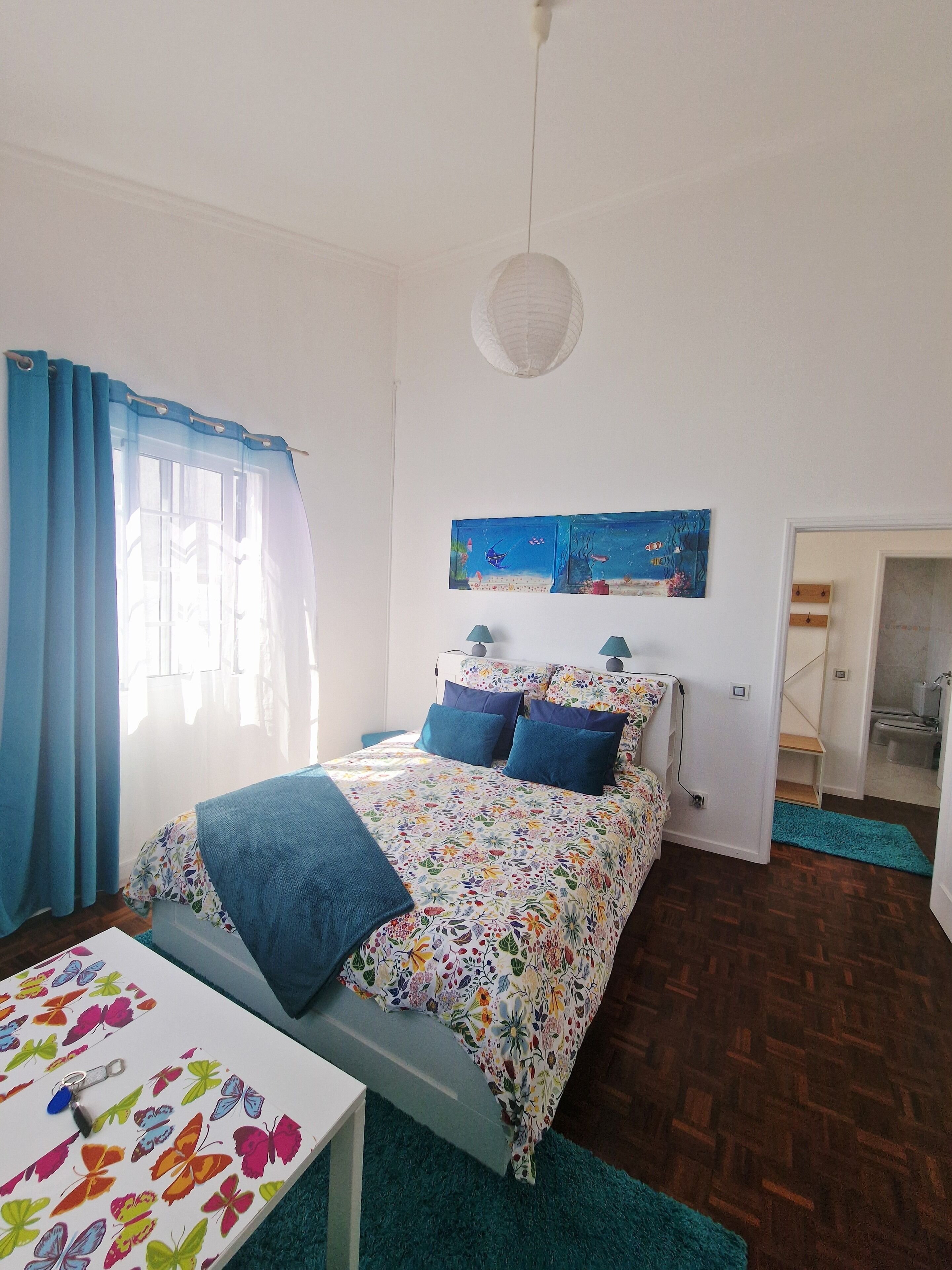 A bedroom with a bed, a table, and a painting on the wall.